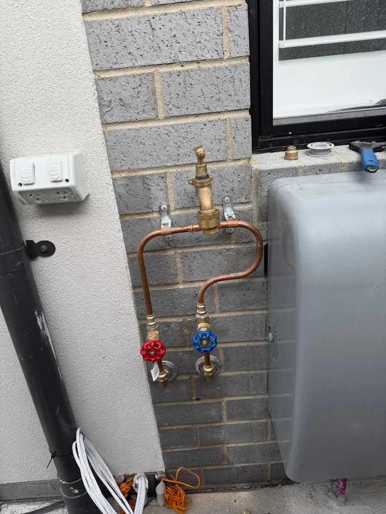 Copper pipework with brass tempering valve and red and blue isolation valves mounted on a brick wall