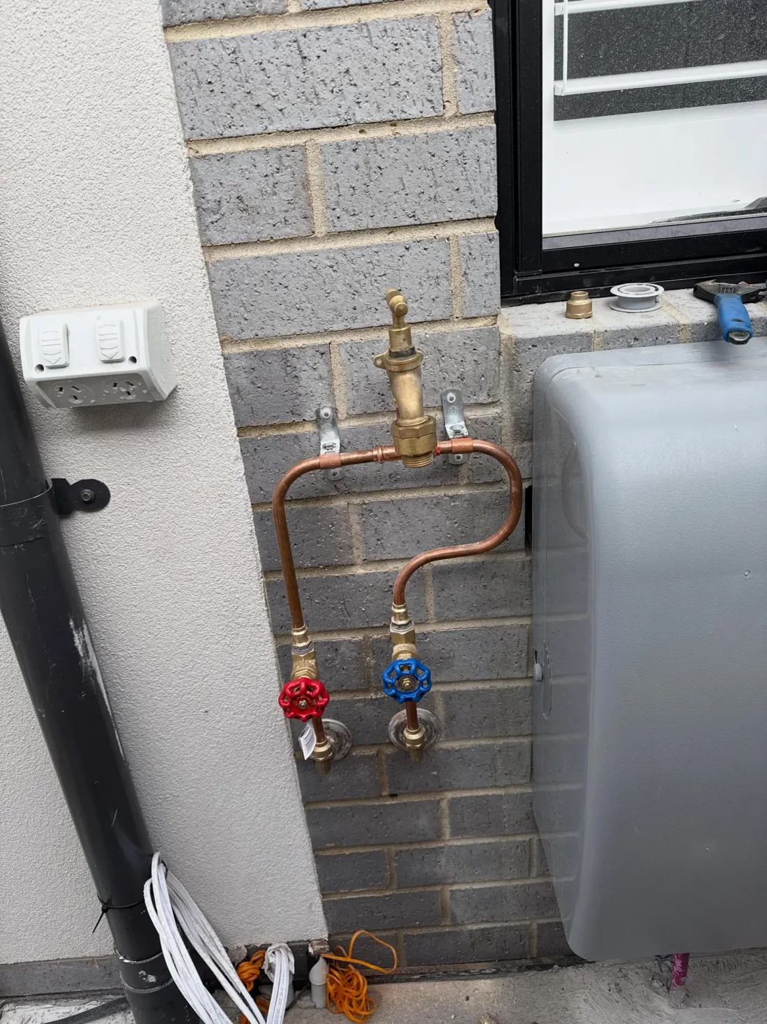Copper pipework with brass tempering valve and red and blue isolation valves mounted on a brick wall