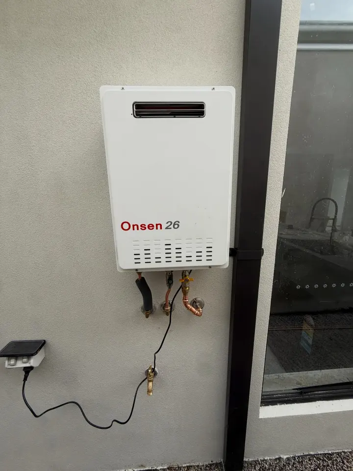 Wall-mounted instantaneous gas hot water unit with copper connections and an isolation valve below it